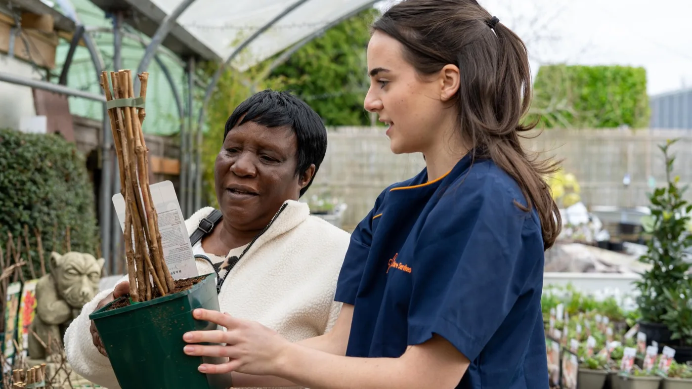 Karis Care support worker in navy uniform out at a garden centre with a woman she supports, choosing plants together in Hampshire